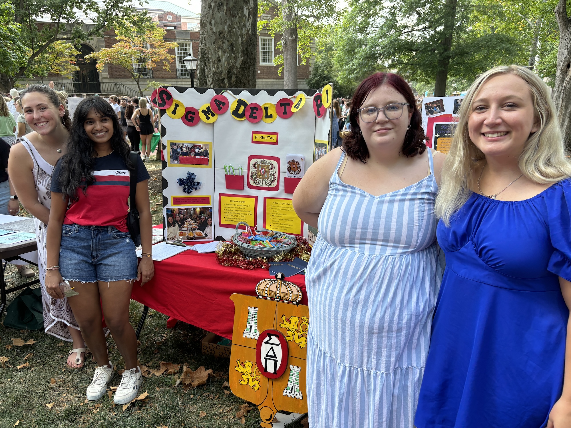 Four students pose for a photo in front of a Sigma Delta Pi poster at the student involvement fair