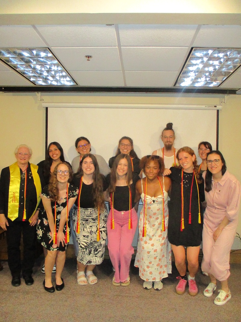 A group of students and faculty members pose for a photo wearing honor cords