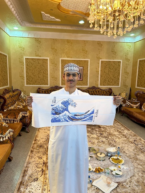 A man holds up a scroll painting showing an ocean's wave