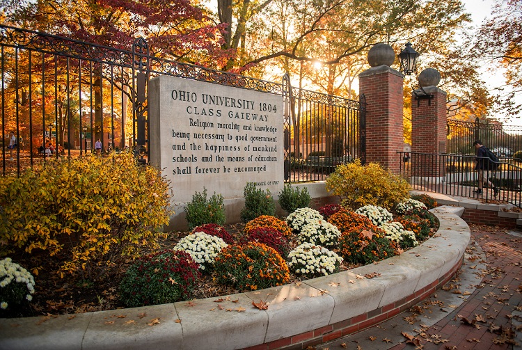 The College Gate is shown on a fall day surrounded by colorful flowers and leaves