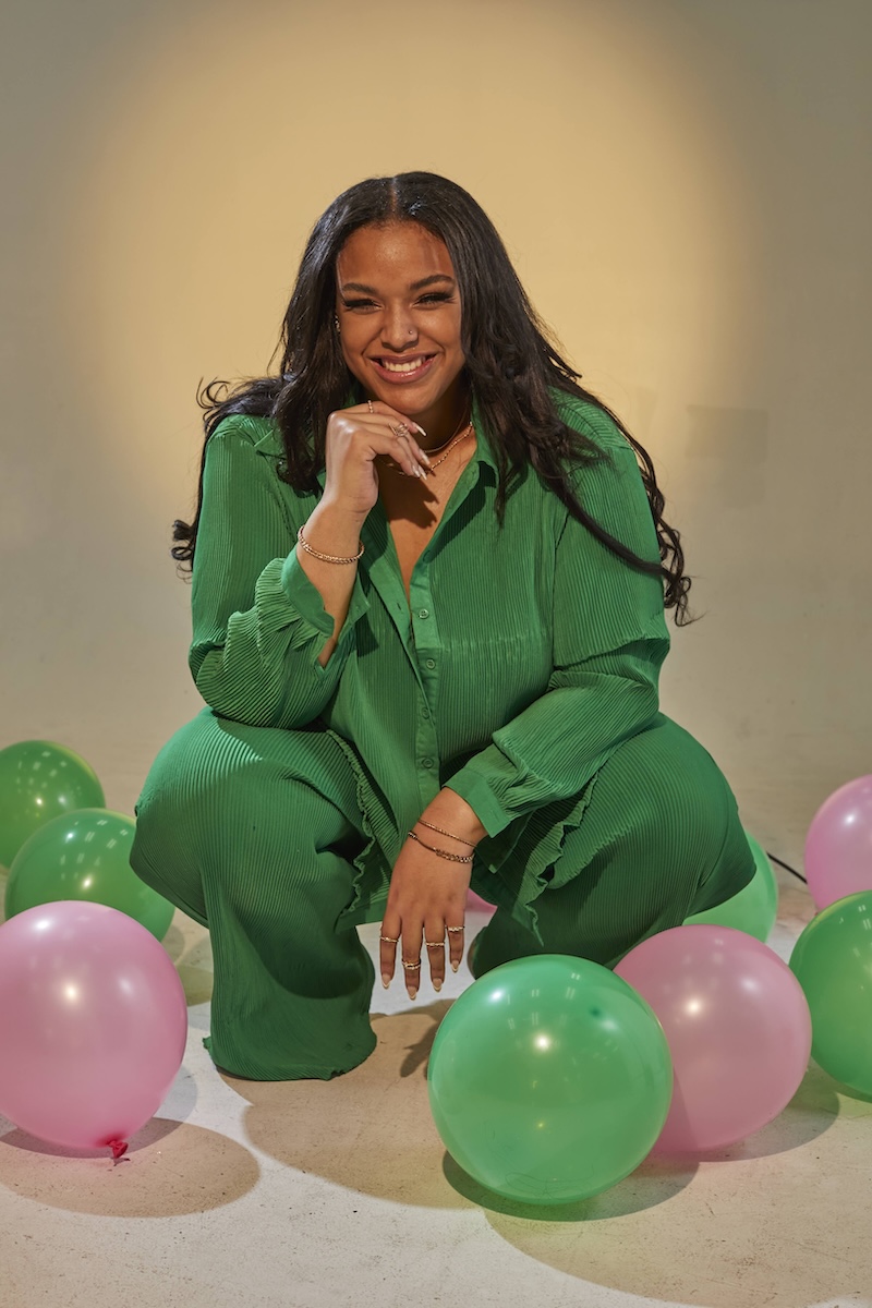 Hadiya Ray posing in a green outfit surrounded by green and pink balloons