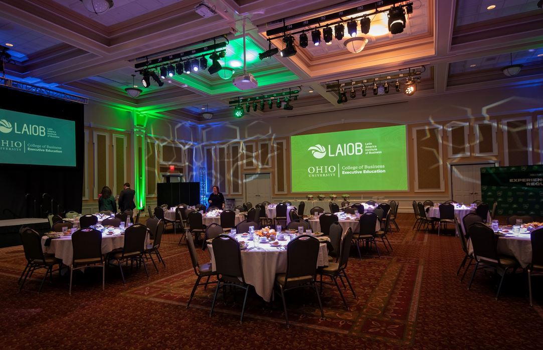 A banquet room with people sitting at tables and a green screen reading "LAIOB."