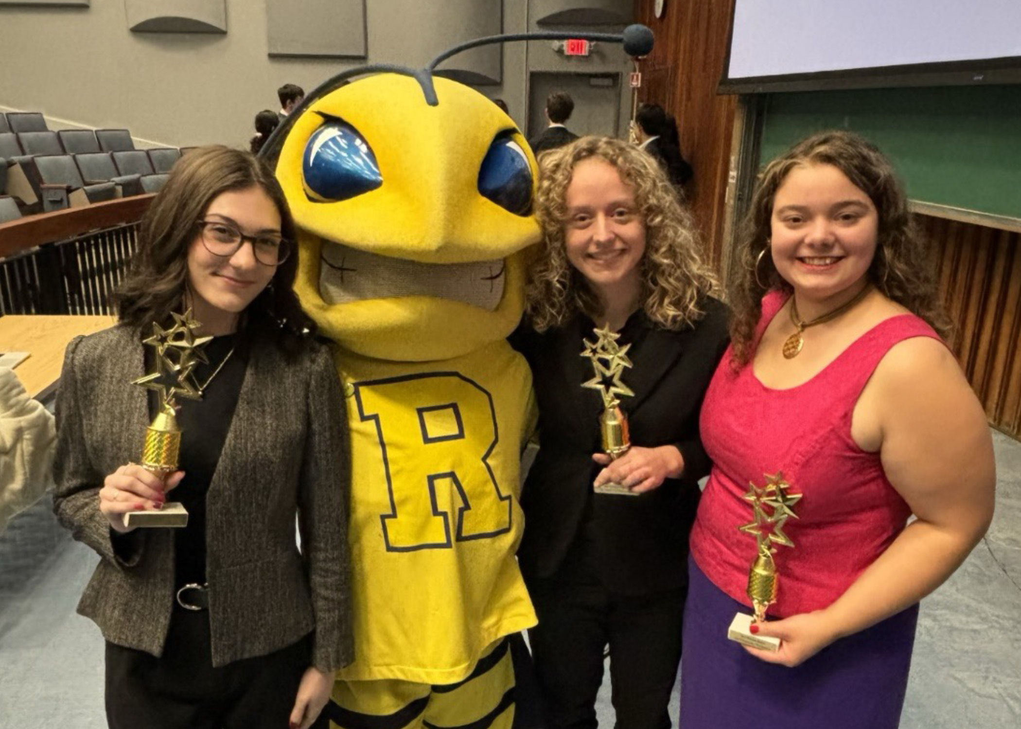 Three students pose with the Rochester mascot, a yellow bee