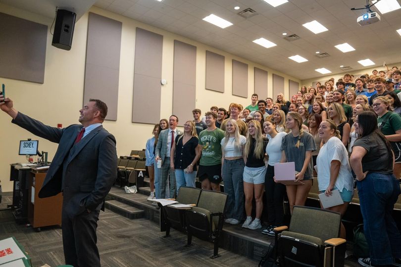 Dr. Rapp taking a selfie with a crowd of students in an auditorium-style classroom.