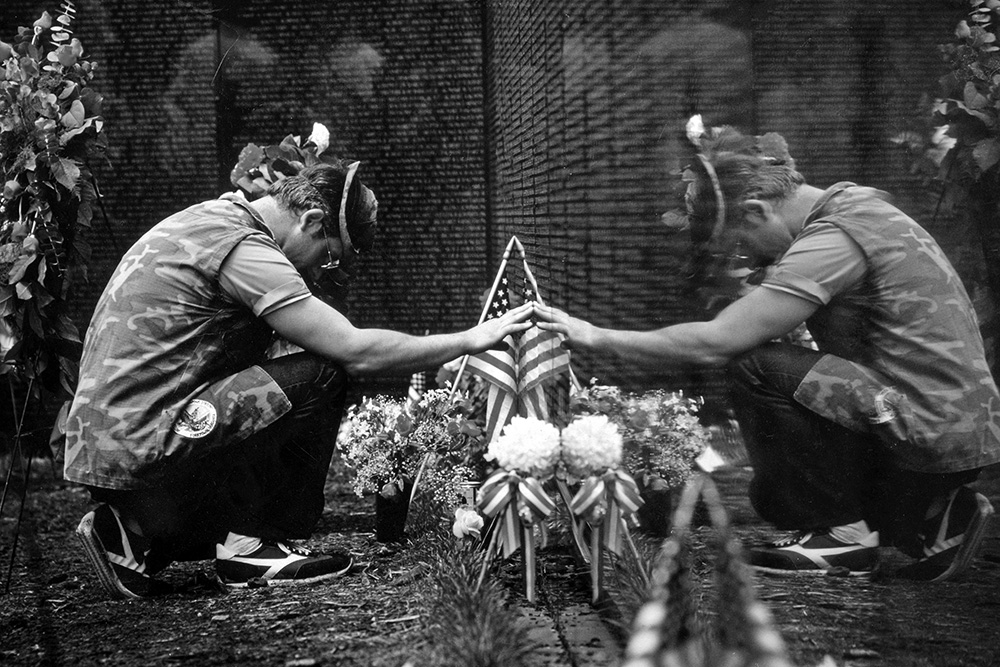 a black and white photo of a man kneeling in front of the vietnam veterans memorial in washington dc