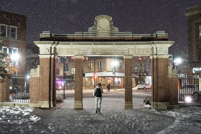 An OHIO student walks through the Alumni Gate toward Uptown Athens on a winter evening when it is snowing