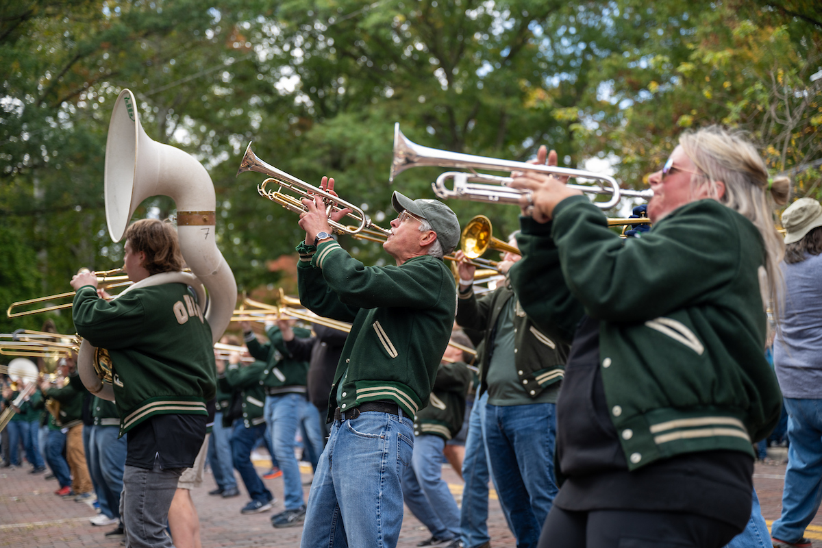 Wearing matching green jackets, a group of marching band alumni perform in the Ohio University Homecoming parade