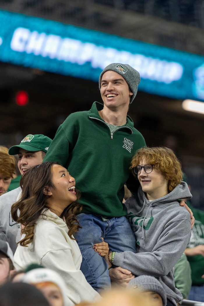 Two students hold a third just off the ground in the stands of the MAC championship football game