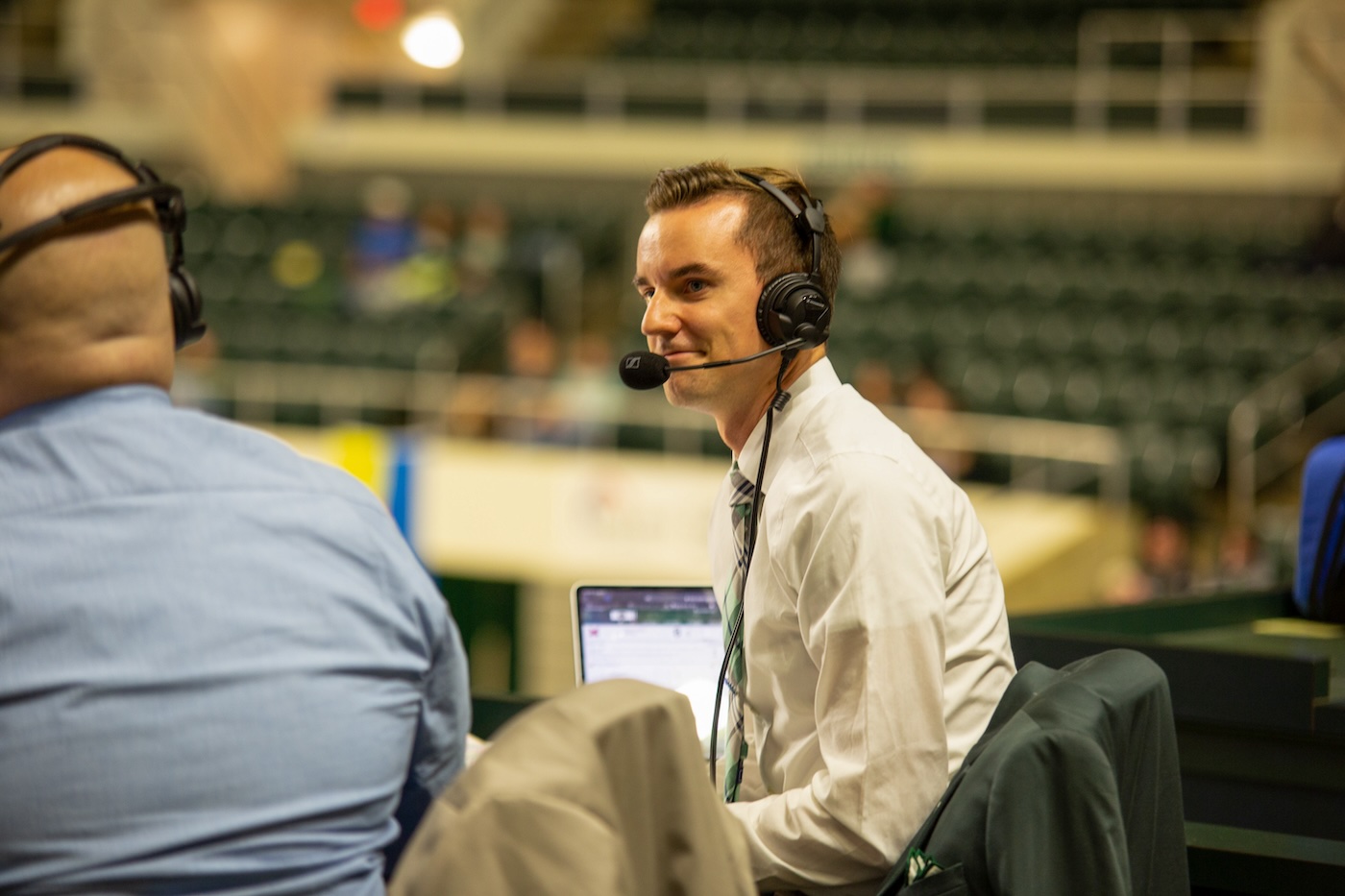 wearing a headset, Jake Hromada smiles in the stands at the Ohio University Convo