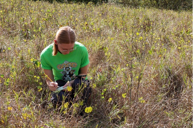 a student crouches in a grassy field, taking notes