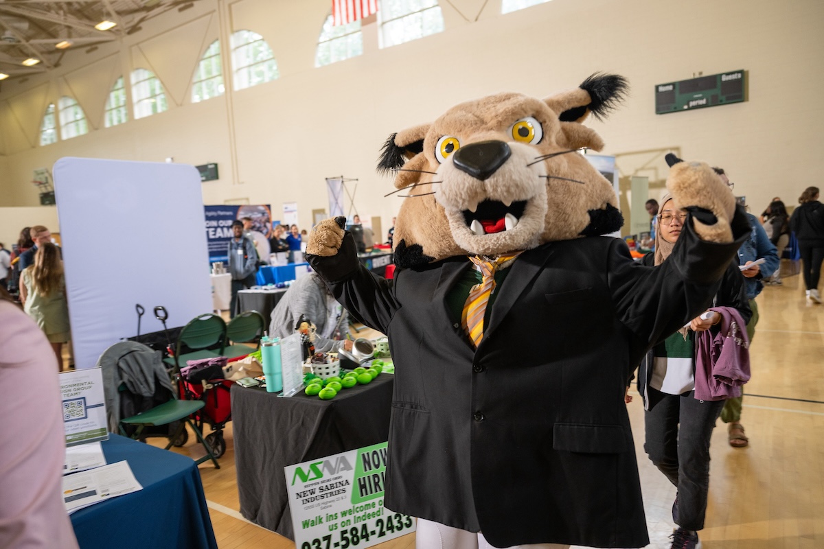 Rufus at the career fair in a suit giving two thumbs up