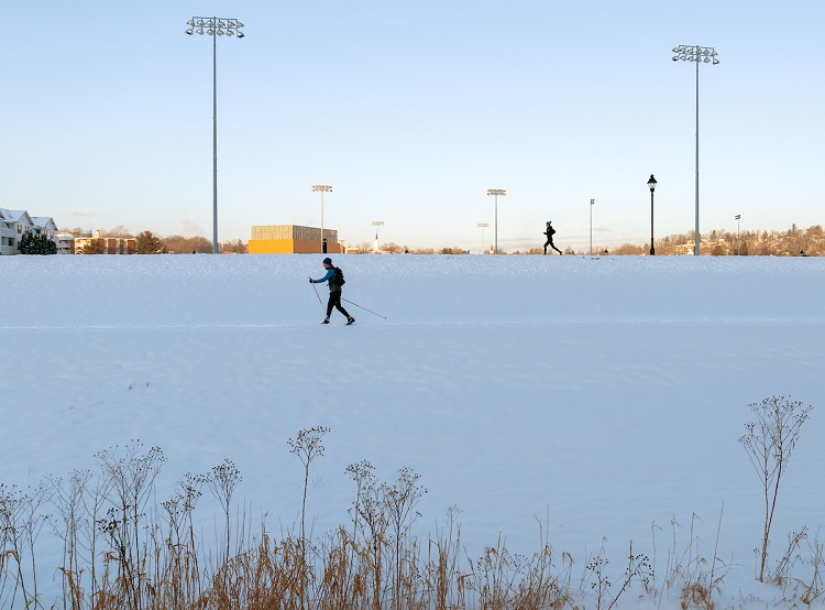 An individual rides a bike on the bike path while another person cross country skis near the bike path on a snowy, January day at Ohio University's Athens Campus