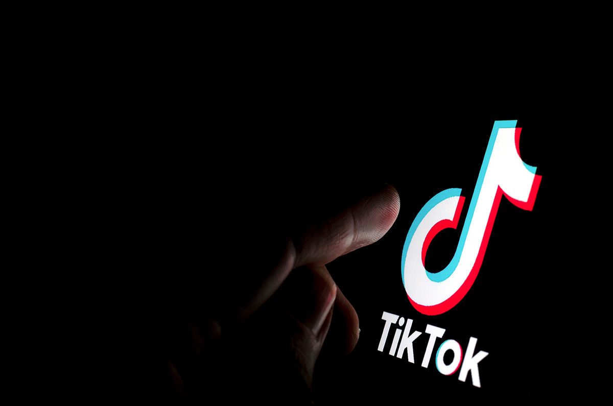 A person's finger points to a digitally lit TikTok logo on a dark background