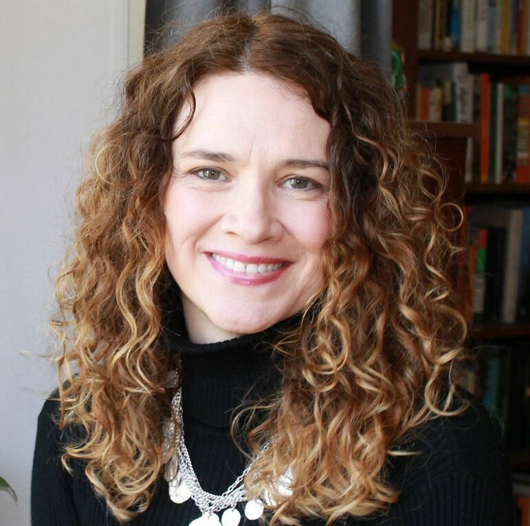 A headshot of a woman with light, curly hair smiling.