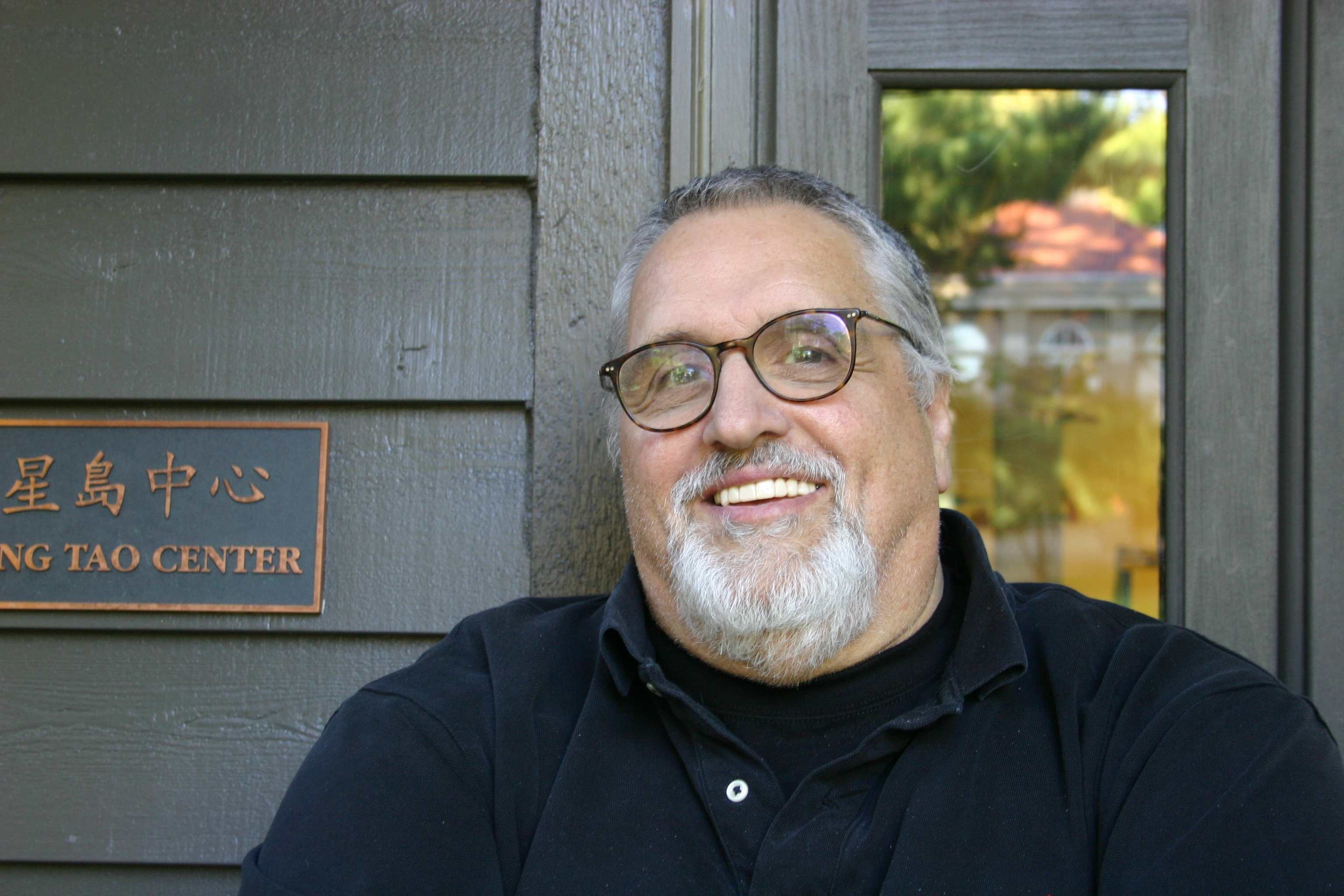 A man with glasses and a black shirt smiling.