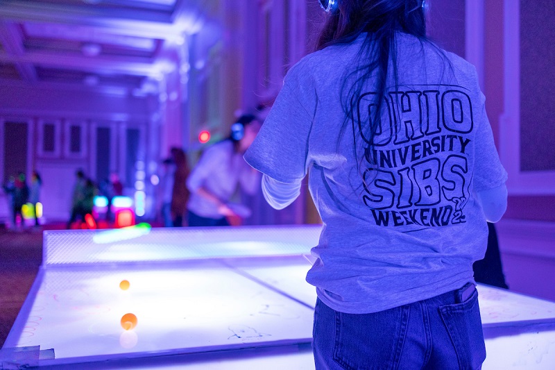 An individual wearing an Ohio University Sibs Weekend shirt plays ping pong at the GLOHIO event