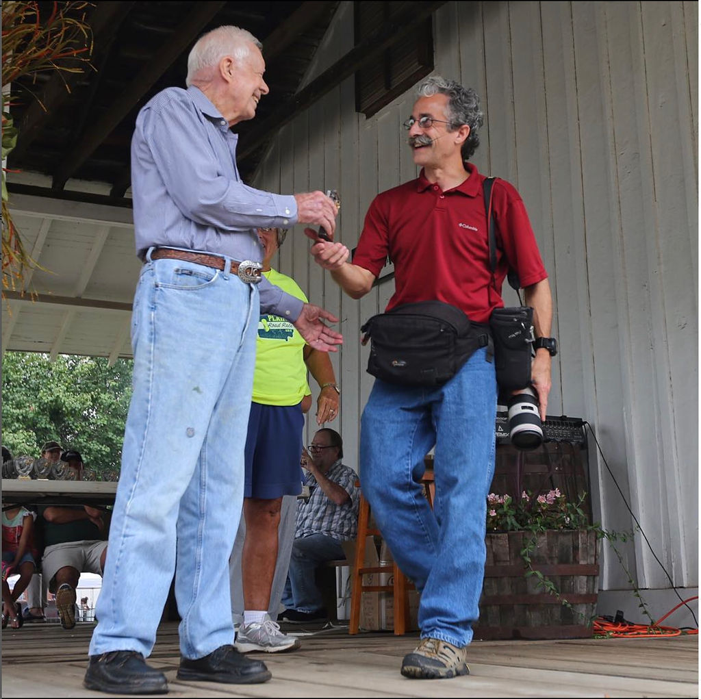 Jimmy Carter shakes hands with Ben Gray, who is carrying a large camera