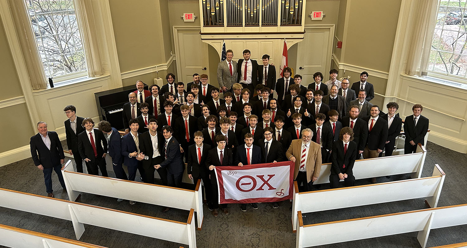 a large group of young men in suits, photographed from above holding a Theta Chi flat in a church