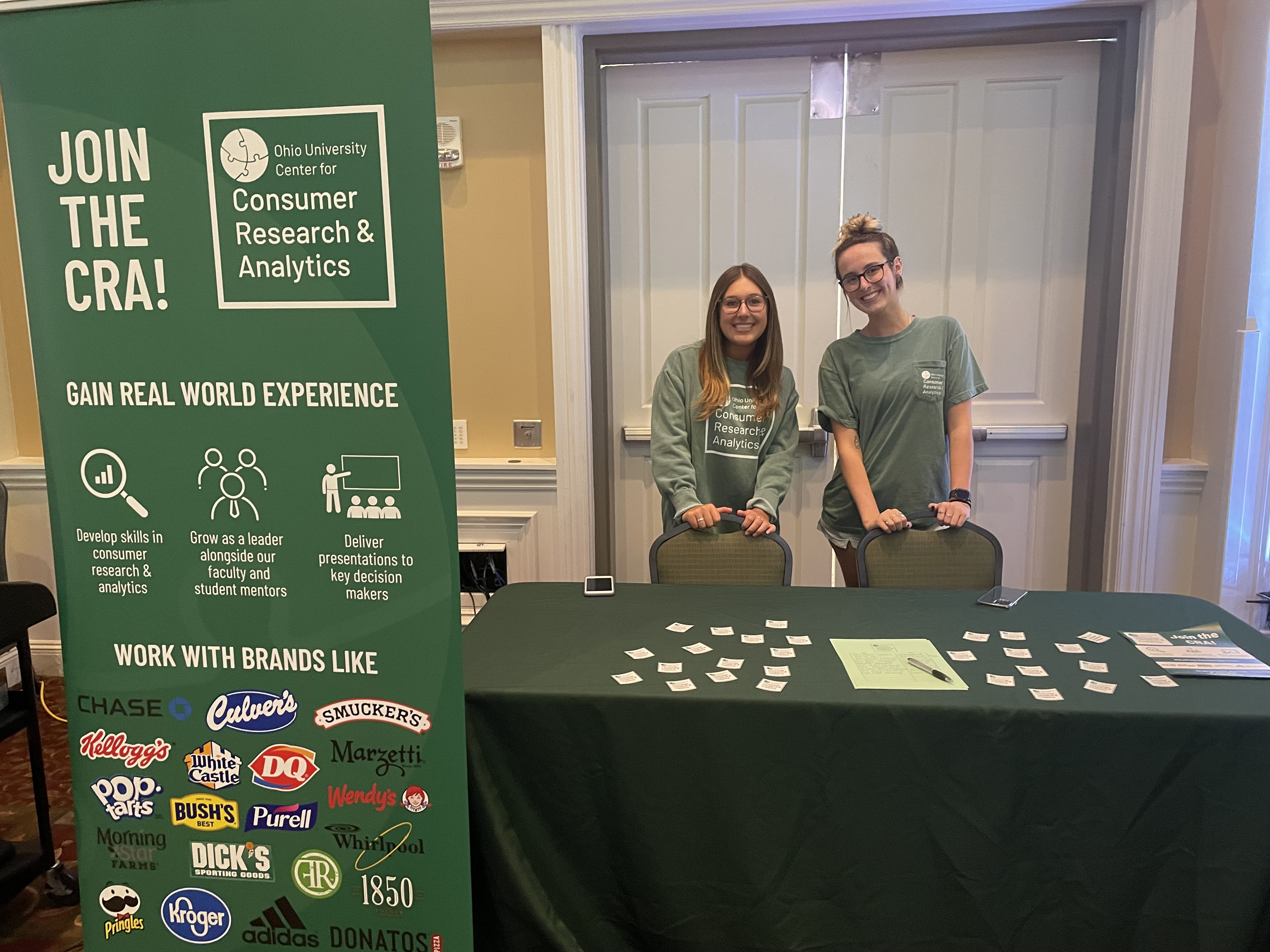 two young women stand behind a table encouraging students to sign up for the Center for Research and Analytics