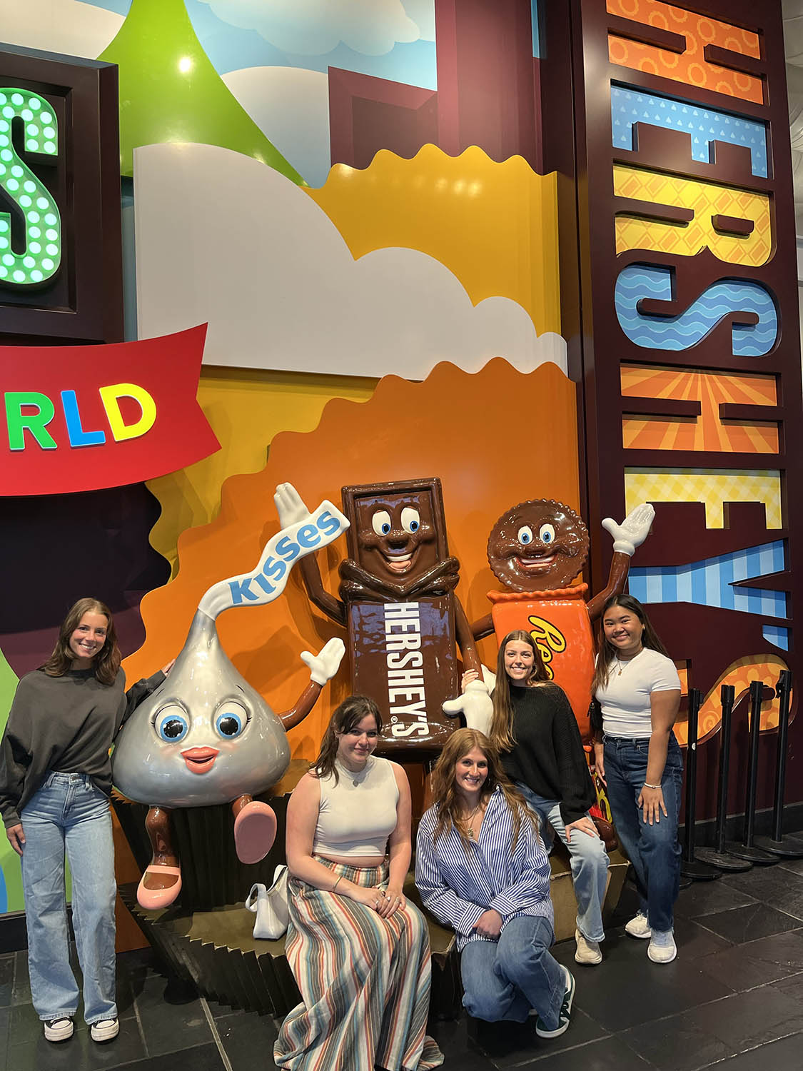 five students in casual attire pose with candy character statues at the Hershey Company headquarters