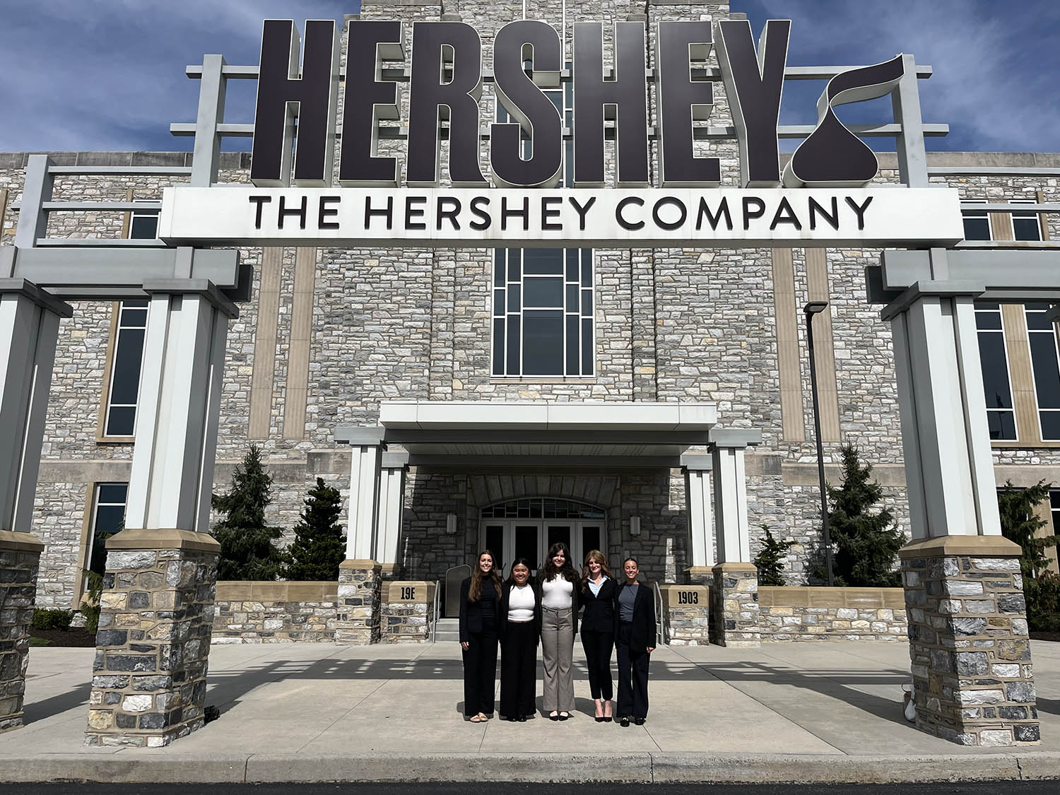 five students in business casual attire stand outside the Hershey Company headquarters