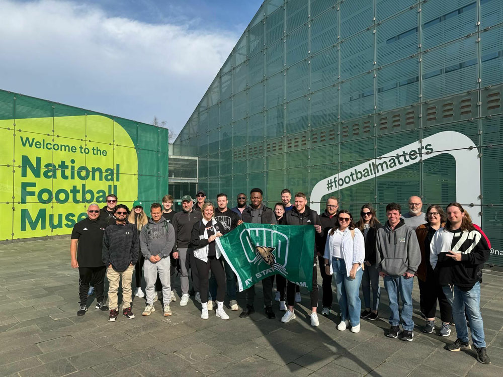 A group of people poses for a photo outside England’s National Football Museum while holding an Ohio University flag.