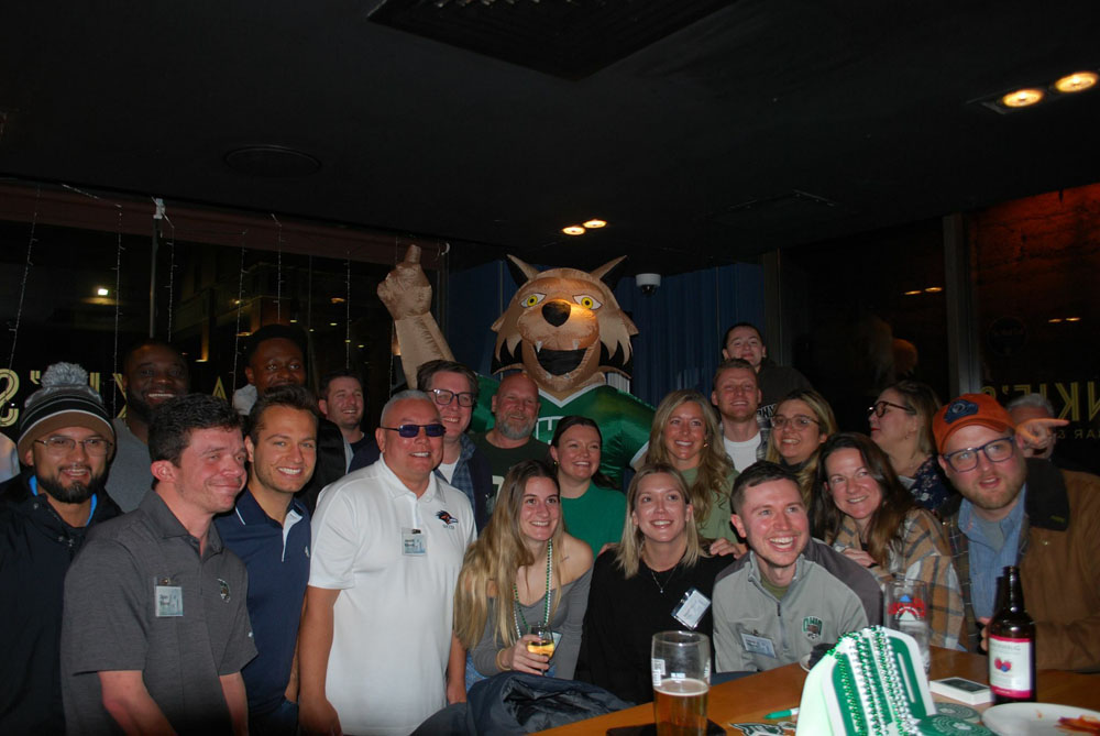 A group of people poses for a photo in a bar with an inflatable Rufus the Bobcat.