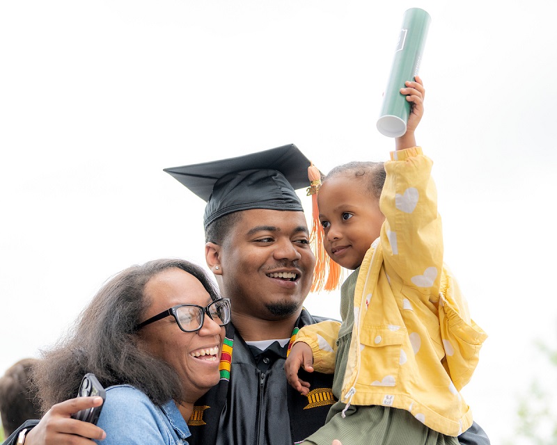 An OHIO student in graduation cap and gown hugs a woman and a young child