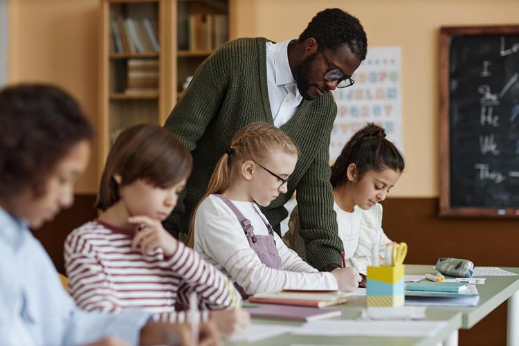A teacher looks over the work of students in a K-12 classroom