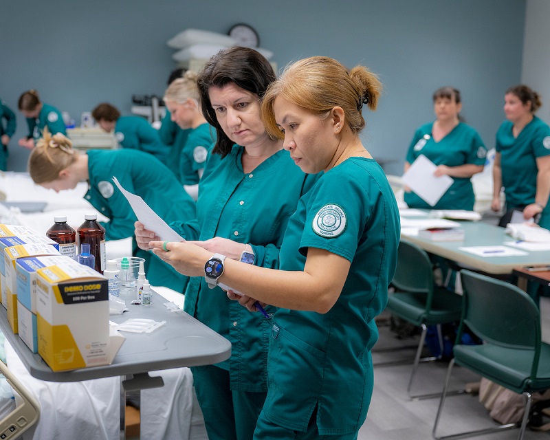 Two nursing students look over a report while other nursing students work in a laboratory setting at OHIO Chillicothe