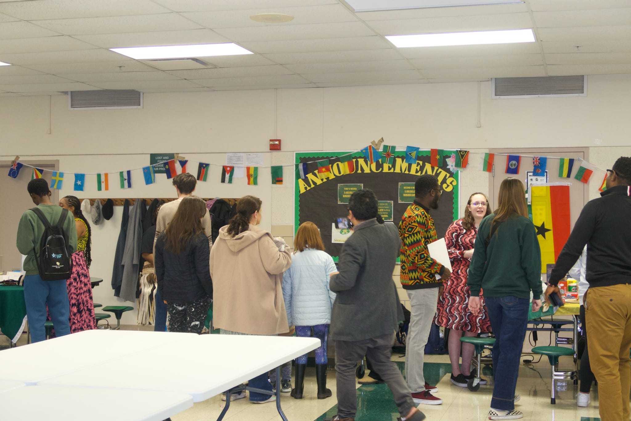 A group of people inside a school surrounding tables.