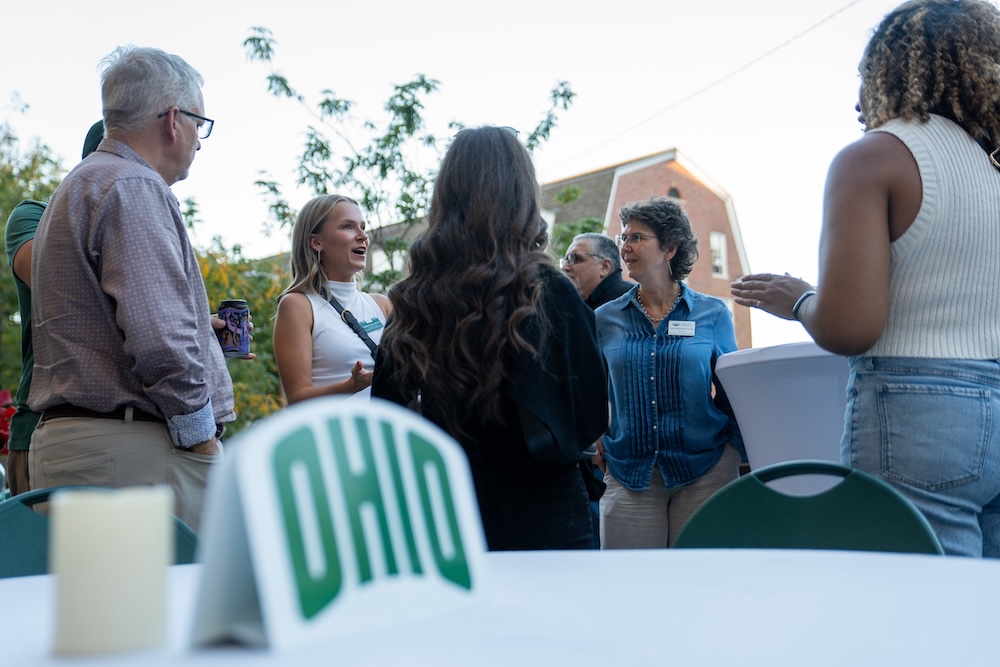 A group of people stand on a patio, talking and smiling