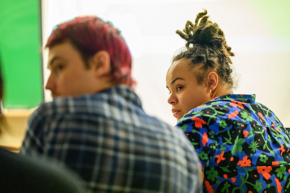 Two students are pictured from behind as they participate in a classroom discussion