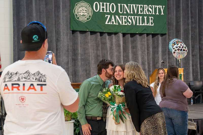 Two family members kiss the cheek of a graduate after the OHIO Zanesville Graduation Recognition Ceremony