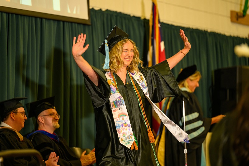 An OHIO graduate smiles and celebrates on stage at the OHIO Lancaster Graduation Recognition Ceremony