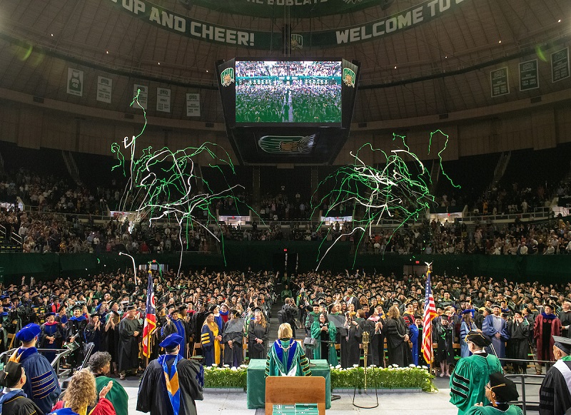 Green and white streamers fall from the Convocation Center ceiling while President Lori Stewart Gonzalez congratulates the graduates at Spring Commencement