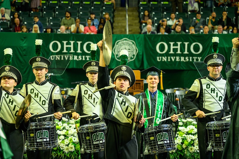 Members of the Marching 110, including one graduate in cap and gown, perform at Spring Commencement in the Convocation Center