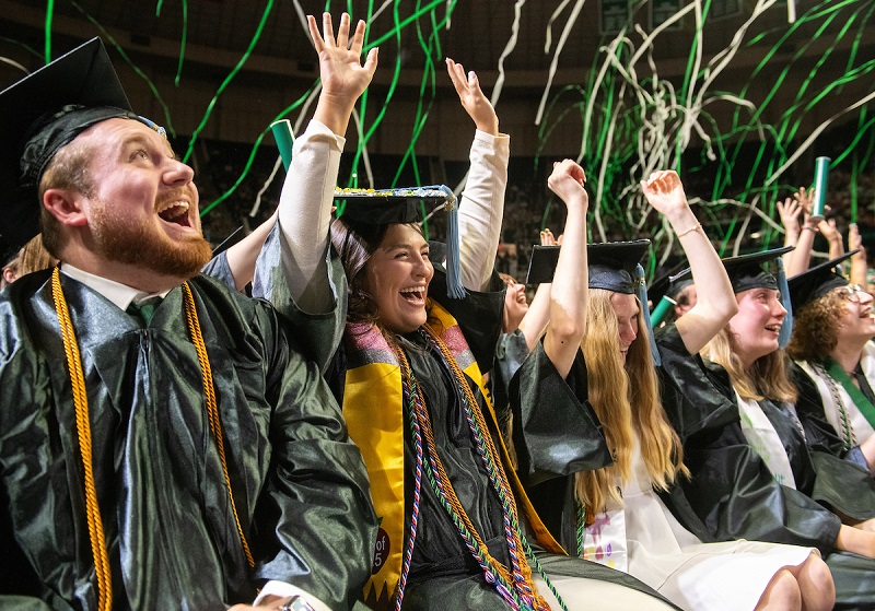 OHIO graduates raise their hands and celebrate as streamers fall over them at Spring Commencement in the Convocation Center