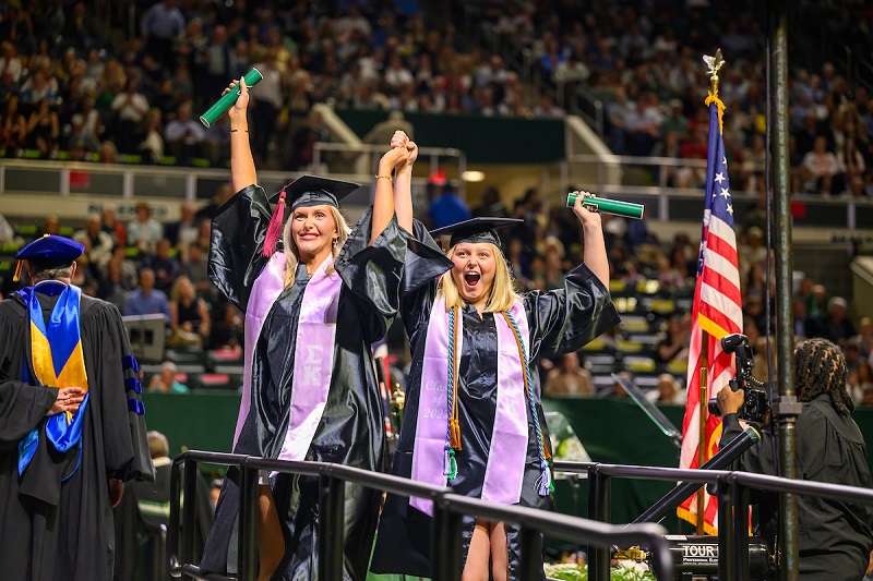 Two OHIO students celebrate after crossing the stage at Spring Commencement in the Convocation Center