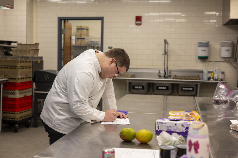 A student taking notes while preparing food.