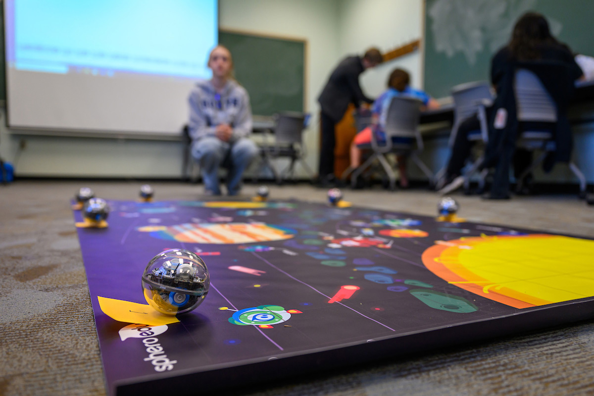 A student studies the game mat, planning the path their Sphero robot will take through the planets.