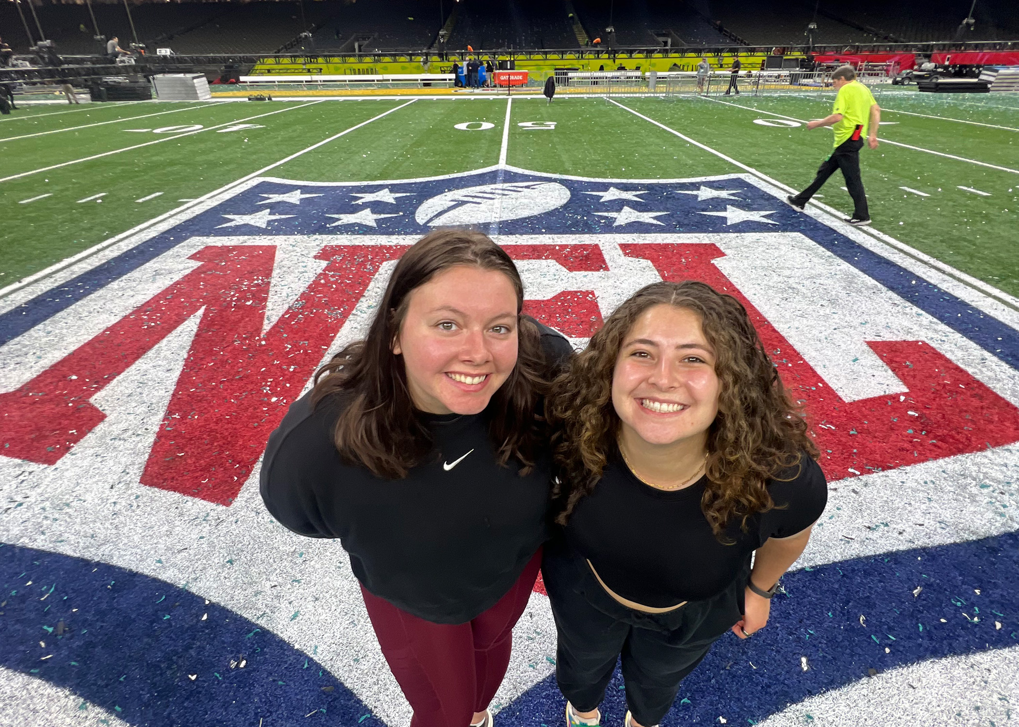 Two women stand on an NFL logo on a football field