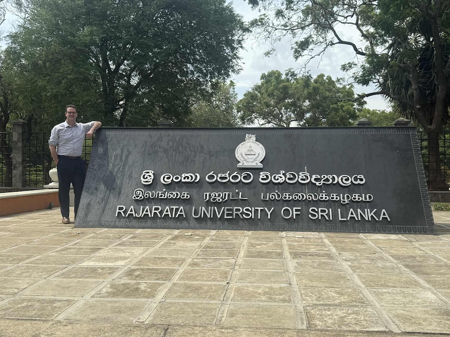 Garrett Field poses with a University sign in Sri Lanka