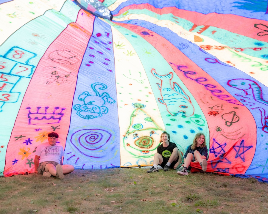 Students sit under a colorful parachute