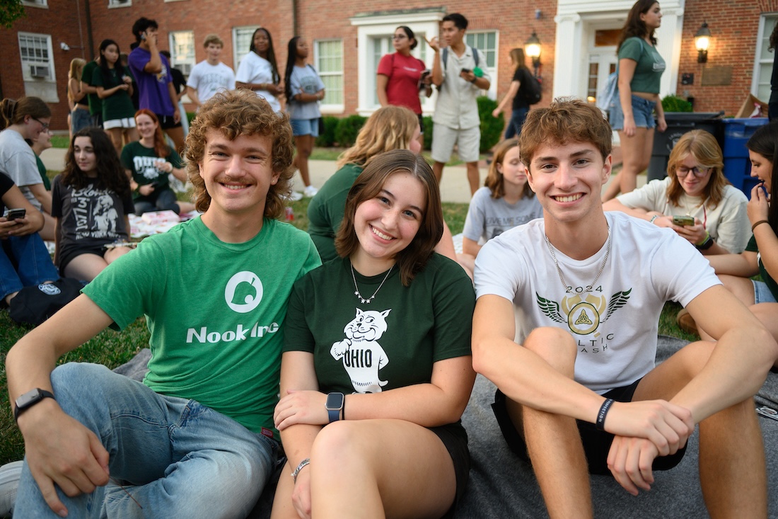Three seated students smile for the camera