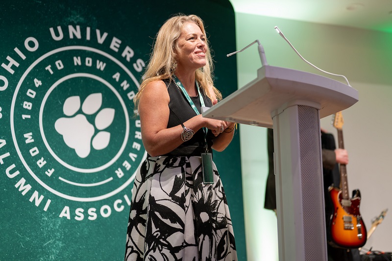Haley Duschinski speaks at the podium while standing in front of a large Ohio University banner at the SISAL dinner