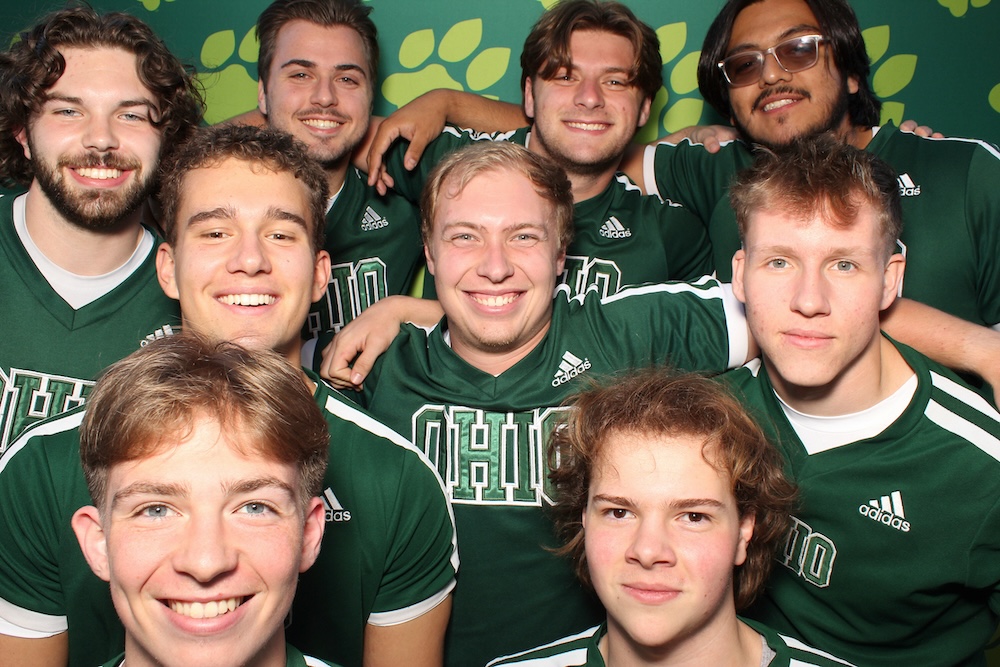 A group of people pose, grinning, for a photo with OHIO pawprints background