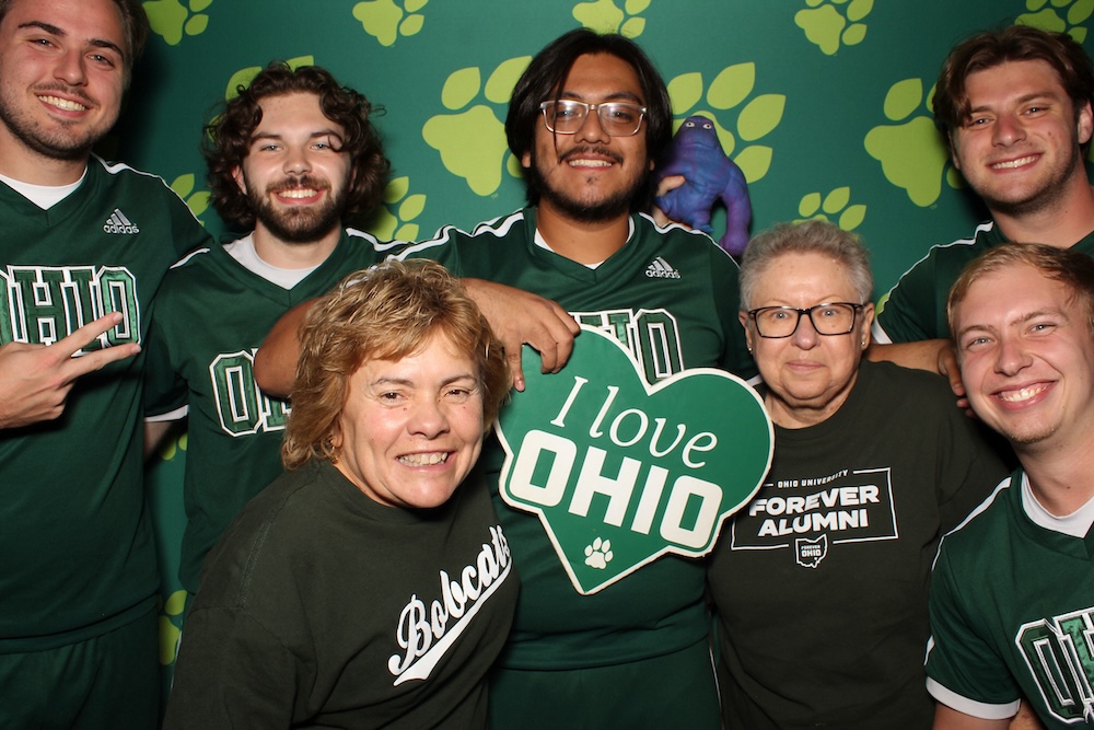 A group of people pose, grinning, for a photo with OHIO pawprints background