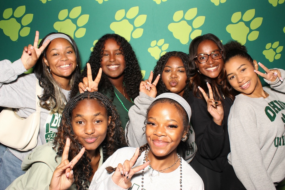 A group of people pose, grinning, for a photo with OHIO pawprints background