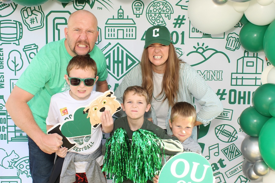 A family poses in Bobcat colors in front of an OHIO themed backgound